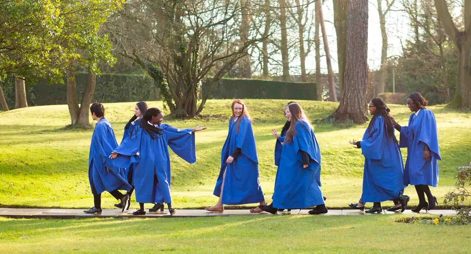 Gli studenti della St. Margaret’s School camminano con toghe blu nel parco del campus.