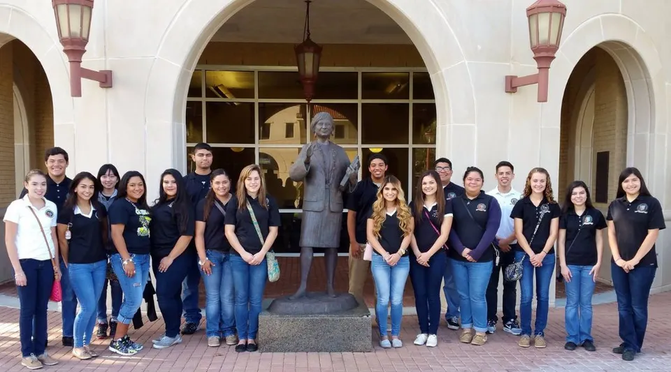 Un gruppo di studenti in posa davanti all'edificio della St. John Paul II High School con archi e luci decorative.