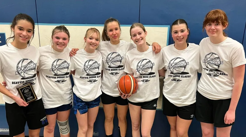 Un gruppo di studentesse della Thousand Islands Secondary School indossa t-shirt bianche con il logo del basket e posa insieme in una palestra.