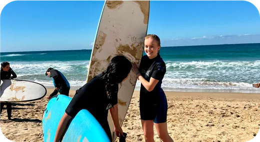 Dos chicas con traje de neopreno sujetando sus tablas de surf en la orilla de la playa