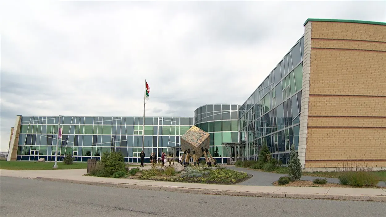 El edificio moderno de la École secondaire publique Gisèle-Lalonde con fachada de vidrio y una escultura frente a la entrada.