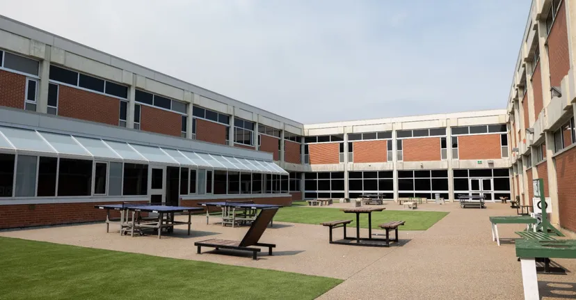 L'edificio moderno della Medicine Hat High School con facciata in mattoni e vetro e un cortile pavimentato con tavoli e sedie.