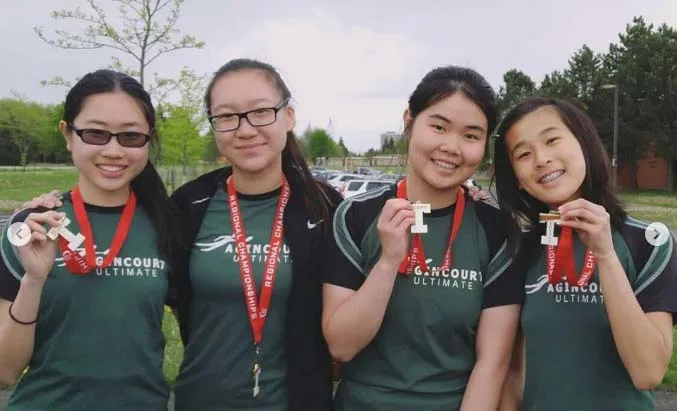 Cuatro alumnas del Dr. Norman Bethune Collegiate Institute llevan camisetas verdes y están juntas en un campo de juego.