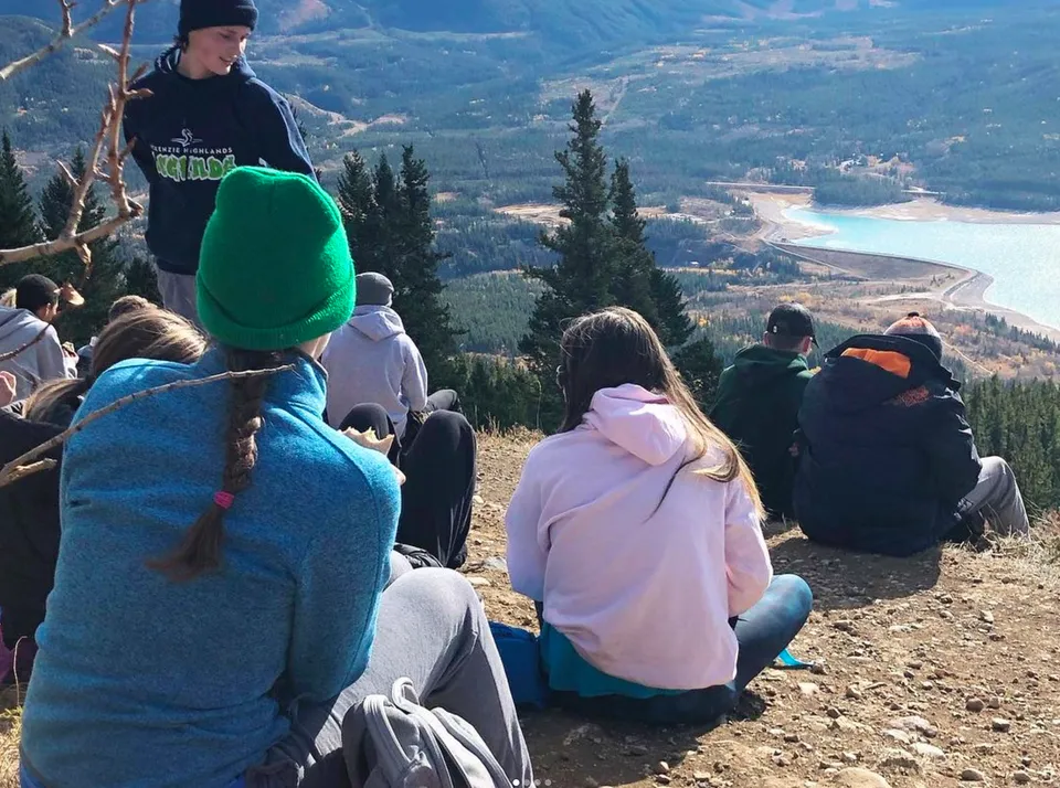 Un gruppo di studenti della Lord Beaverbrook High School si trova su una collina e osserva un paesaggio montano con una strada.