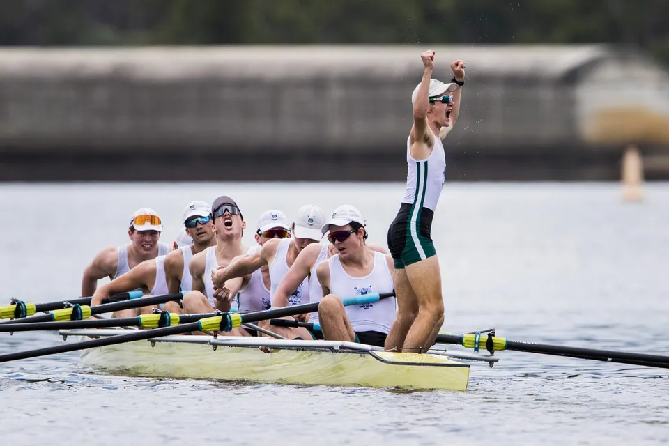 Un gruppo di canottieri festeggia in barca sull'acqua al Brisbane Boys' College.