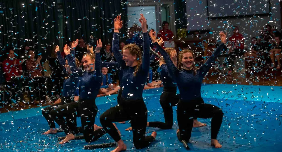 Studentesse della St. Mary's School festeggiano a braccia alzate su un tappeto blu sotto una pioggia di coriandoli.