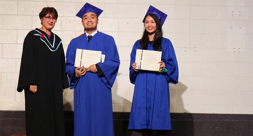 Tre diplomati del L'Amoreaux Collegiate Institute posano con i loro diplomi davanti a una parete bianca.