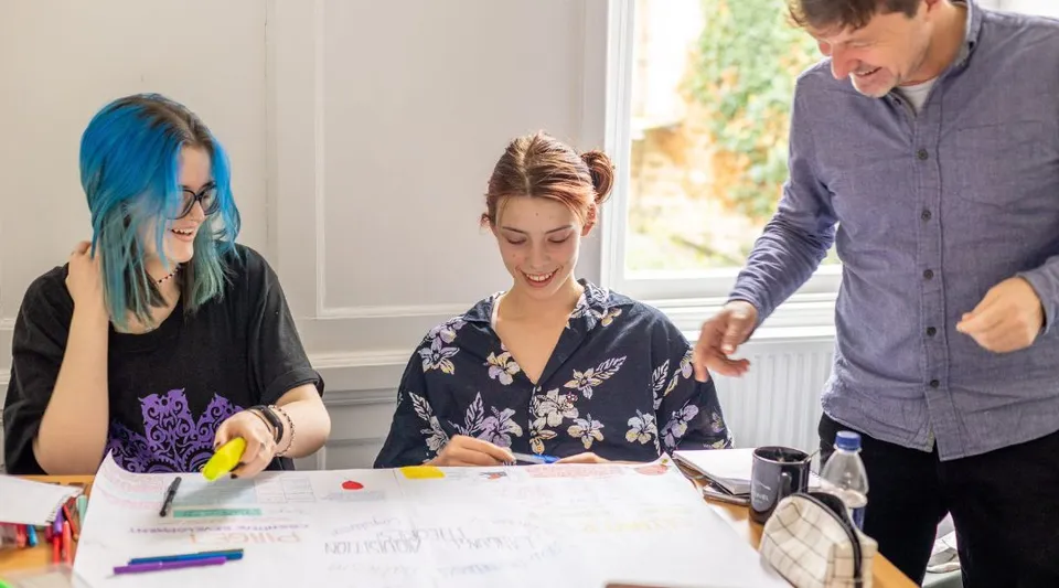 Studenti della Bath Academy lavorano insieme a un progetto d'arte al tavolo con diversi materiali.