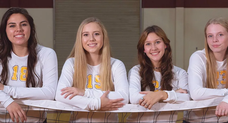 Quattro studentesse della Kings Christian School in maglia bianca con il numero 13 si trovano insieme in un ambiente sportivo davanti a una recinzione metallica.