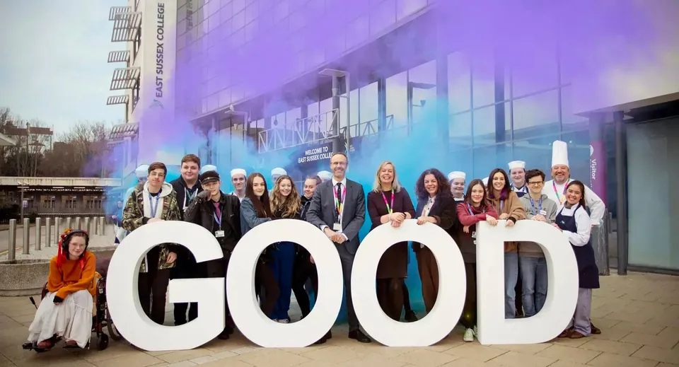 Un gruppo di studenti e insegnanti dell'East Sussex College posa dietro a grandi lettere bianche che formano la parola GOOD.