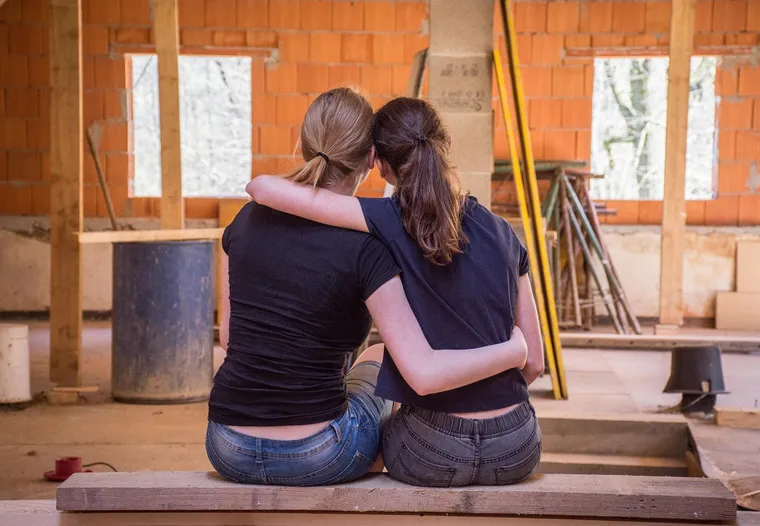 Zwei junge Frauen sitzen Arm in Arm auf einem Brett in einem Rohbau
