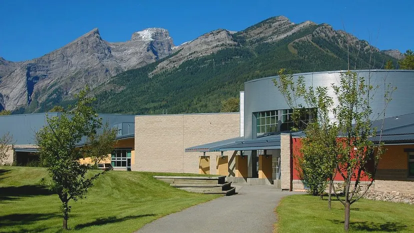 L'edificio moderno della Fernie Secondary School si trova davanti a un prato verde con le montagne sullo sfondo sotto un cielo limpido.