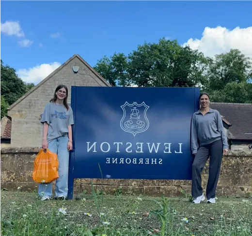 Theresa und eine Mitschülerin am Schild der Leweston School in Sherborne, England
