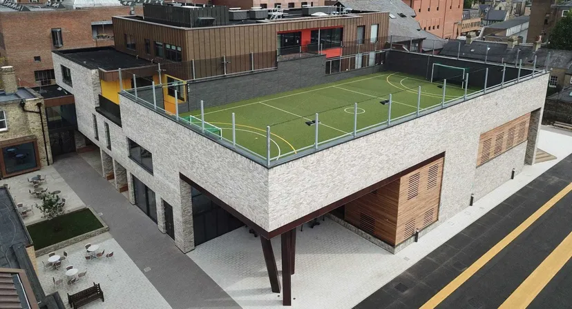 L'edificio a più piani della Stephen Perse Foundation con un campo da calcio sul tetto in un contesto urbano.