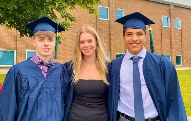 Tres estudiantes de la Sir Wilfred Laurier Secondary School celebran su graduación frente a un edificio de ladrillo.