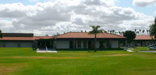Un edificio a un piano con tetto in tegole e palme nel campus della Bethel Christian Schools sotto un cielo nuvoloso.