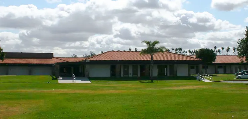 Un edificio a un piano con tetto in tegole e palme nel campus della Bethel Christian Schools sotto un cielo nuvoloso.