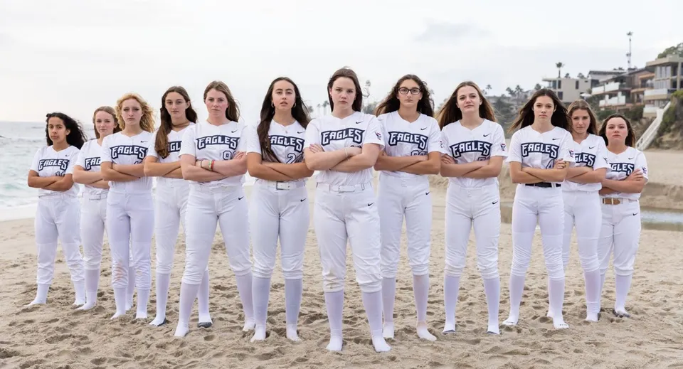 Un gruppo di studentesse in divisa bianca con la scritta Eagles si trova sulla spiaggia sotto un cielo nuvoloso vicino al campus della Capistrano Valley Christian.