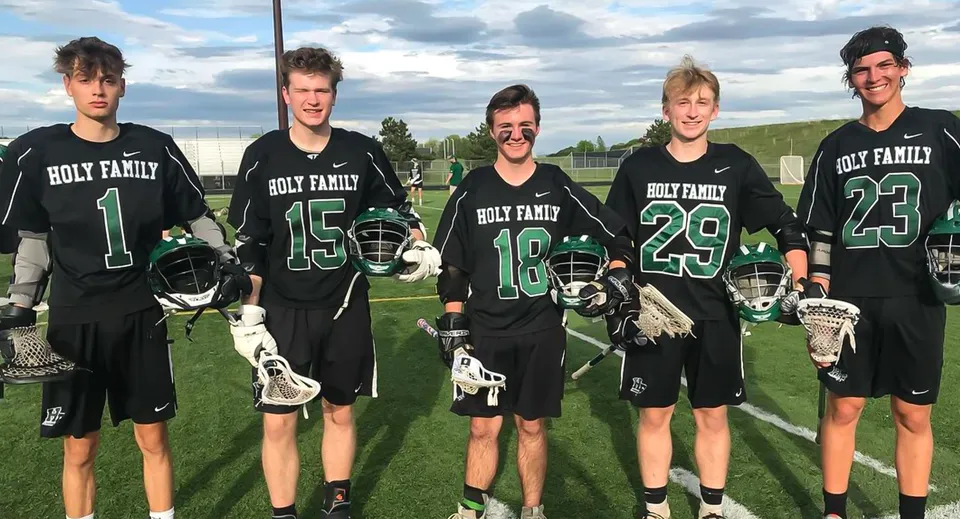 Un gruppo di studenti della Holy Family Catholic High School si trova in divisa su un campo sportivo sotto un cielo nuvoloso.