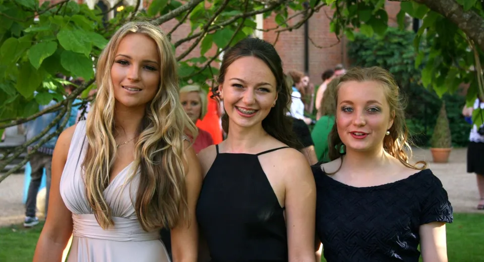 Tre studentesse della Sherborne Girls' School sono insieme in un giardino con vegetazione lussureggiante e alberi.