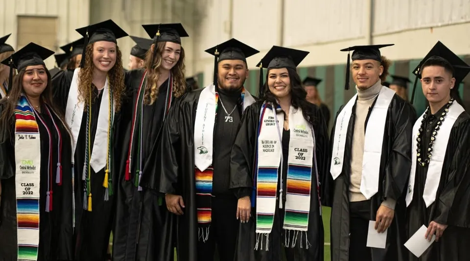Un gruppo di neolaureati in toga posa insieme davanti a uno sfondo semplice nel campus della Central Methodist University.