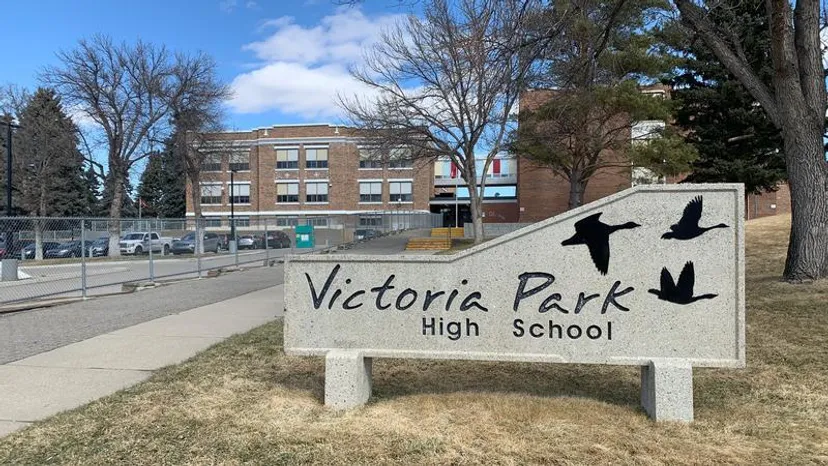 Un cartello della Victoria Park High School con un edificio in mattoni e alberi sullo sfondo.