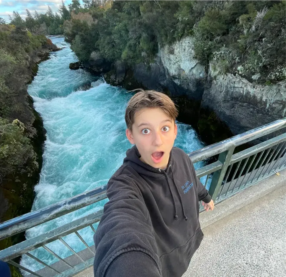 Junge macht ein Selfie auf einer Brücke über einen türkisen Fluss mit Hochwasser in Neuseeland