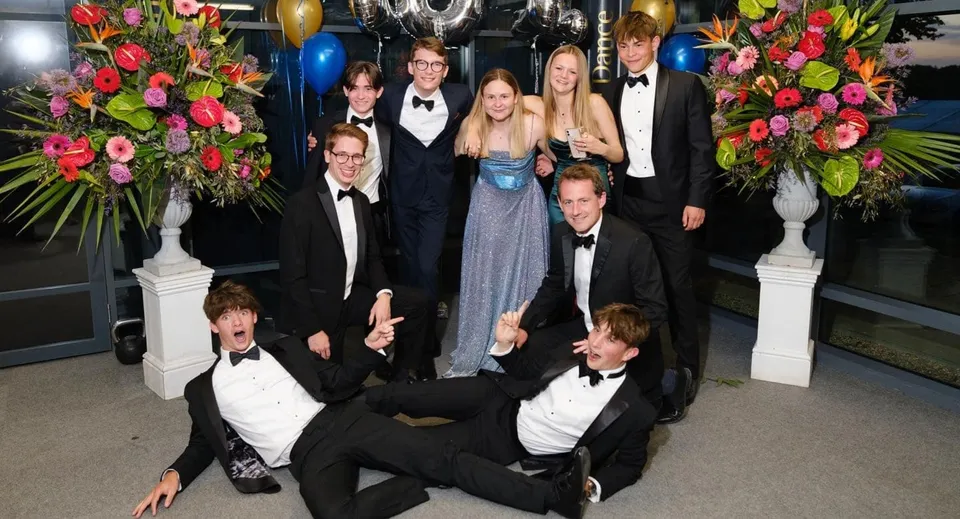 Un gruppo di persone vestite in modo formale posa a un evento con composizioni floreali nel campus della Royal Russell School.