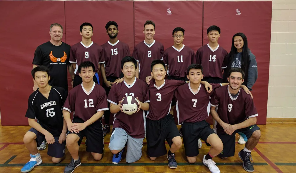 La squadra di pallavolo dell'Albert Campbell Collegiate Institute in posa insieme nella palestra davanti a una parete rossa.