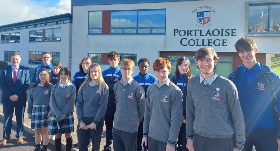 Studenti del Portlaoise College davanti a un moderno edificio scolastico con ampie finestre.