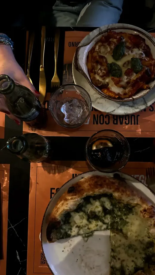 Vista dall'alto di un tavolo con pizze e bevande in un ristorante, tovagliette con scritte in spagnolo