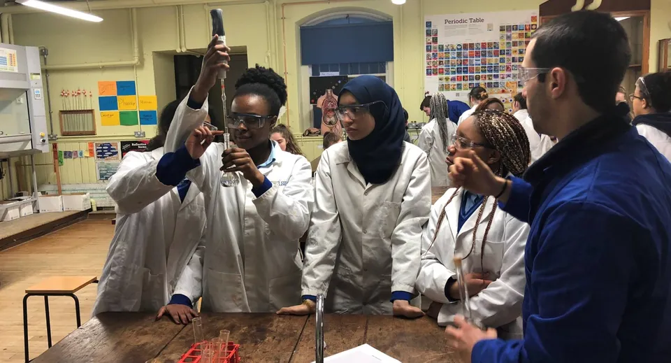 Studenti e studentesse del Loreto College Mullingar lavorano in camice bianco da laboratorio in un'aula con materiali scientifici.
