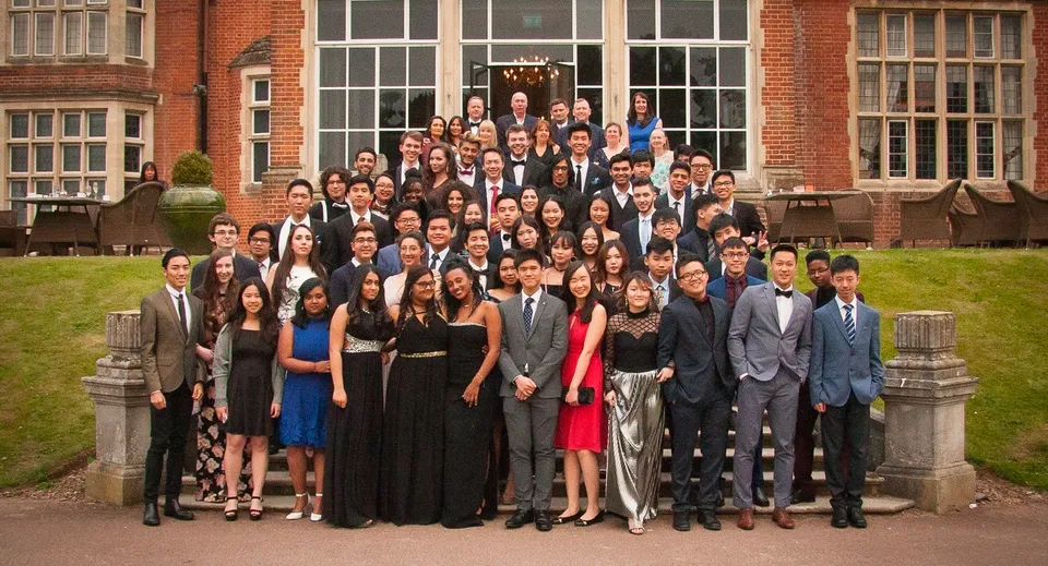 Un gruppo di studenti del Cambridge Tutors College si riunisce in abiti formali davanti a un edificio storico in mattoni.