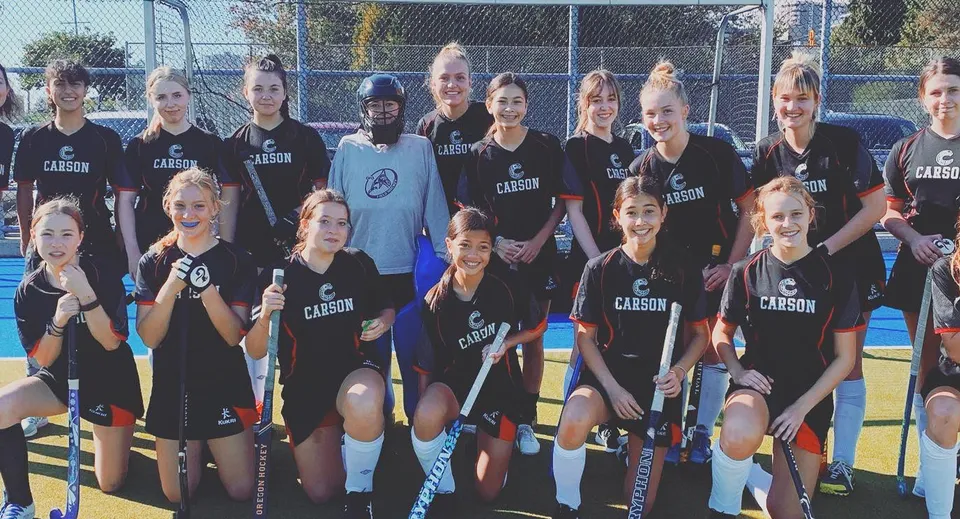 Un gruppo di giovani atlete posa insieme sul campo sportivo della Carson Graham Secondary School.