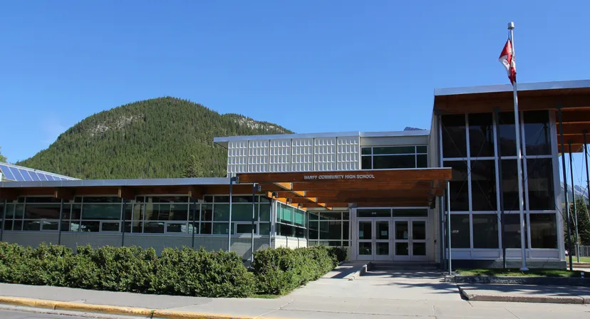 Edificio moderno della Banff Community High School con bandiera canadese davanti a una montagna boscosa.