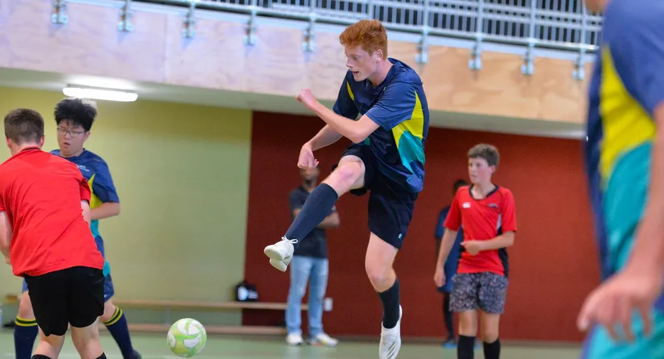 Uno studente dell'ACG Tauranga gioca a calcio nella palestra, circondato da altri studenti.