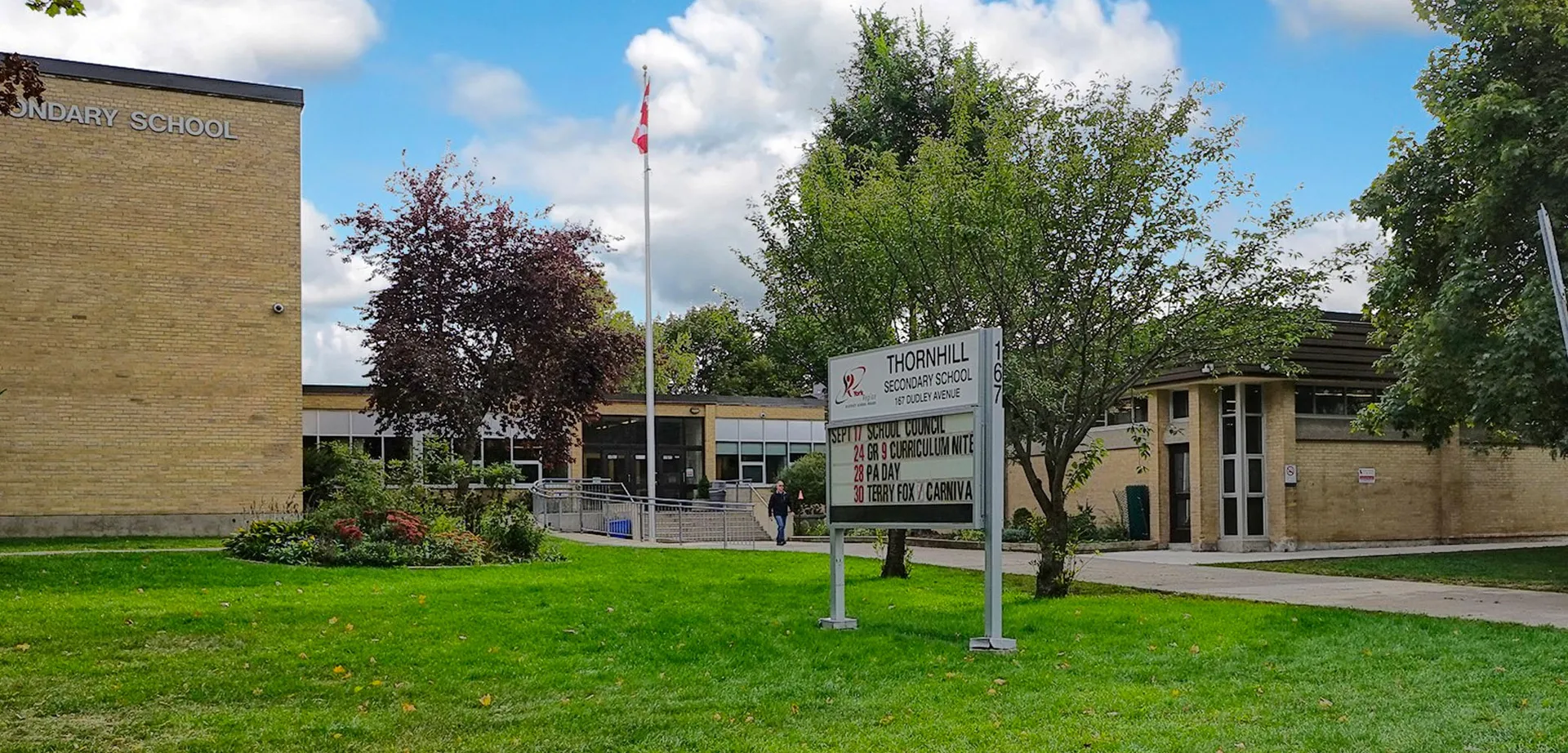 L'edificio scolastico della Thornhill Secondary School è circondato da alberi e in primo piano c'è un prato con una bandiera canadese.