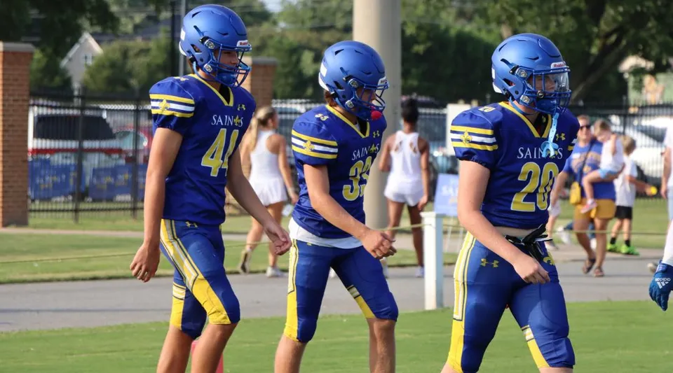 Tre giocatori di calcio della Nansemond-Suffolk Academy sono in piedi sul prato davanti a un edificio scolastico.