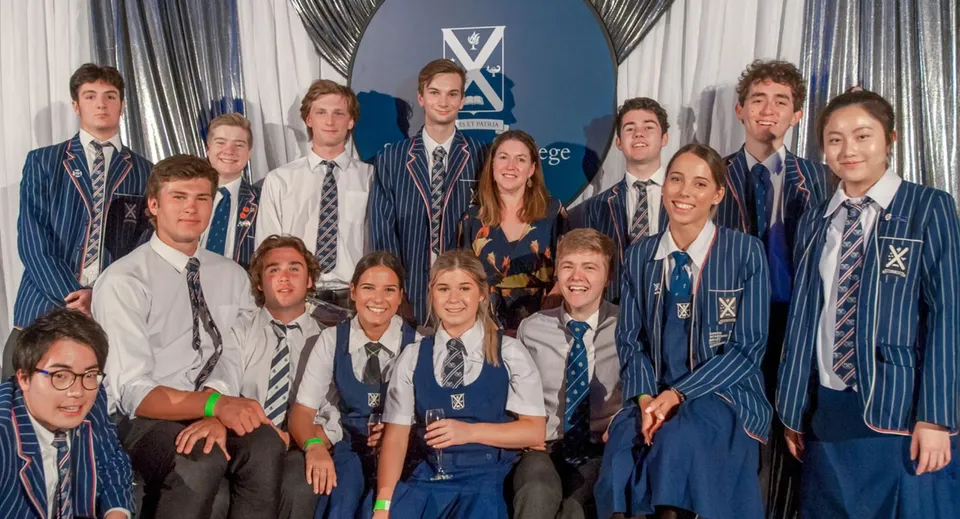Un gruppo di studenti in divisa scolastica posa davanti a uno sfondo con il logo del St. Andrew's College.