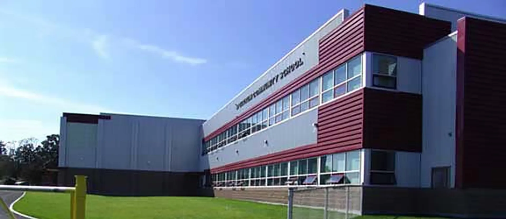 L'edificio moderno a più piani della Spectrum Community Secondary School, con facciata rossa e bianca, è circondato da un prato verde.