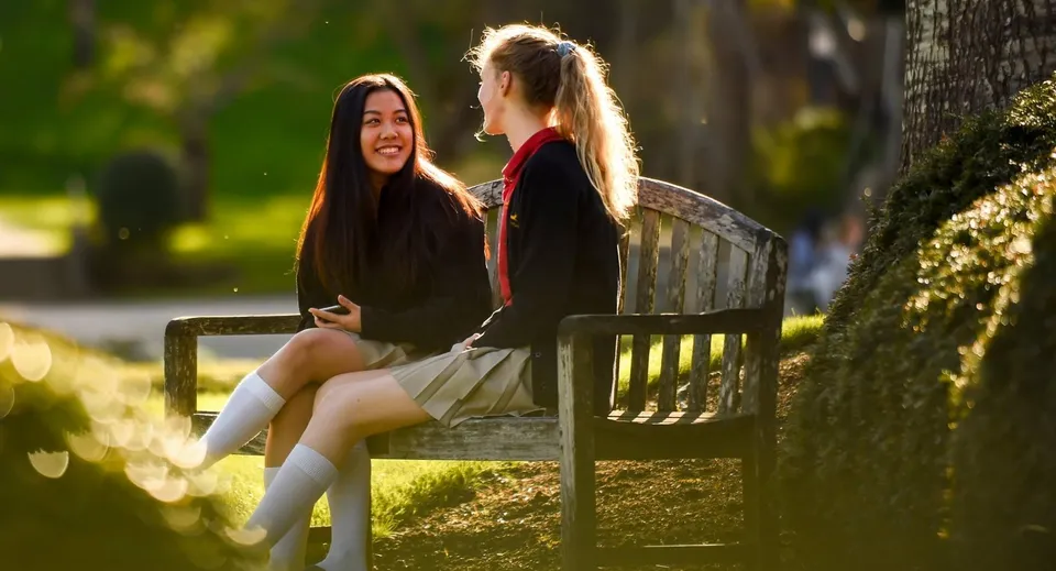 Due studentesse della Shawnigan Lake School conversano sedute su una panchina di legno all'aperto.