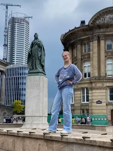 Chica posando junto a la estatua de la reina Victoria en una plaza del centro de la ciudad