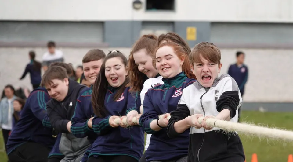 Studenti della Palmerstown Community School festeggiano insieme su un campo sportivo davanti a un edificio scolastico.