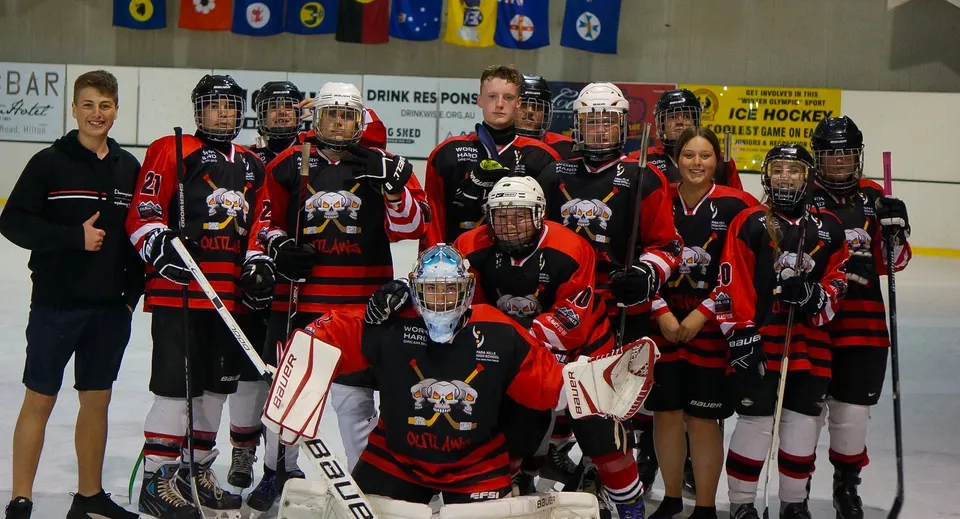 Un gruppo di studenti di hockey della Para Hills High School posa in una pista di pattinaggio su ghiaccio con gli striscioni della squadra sullo sfondo.