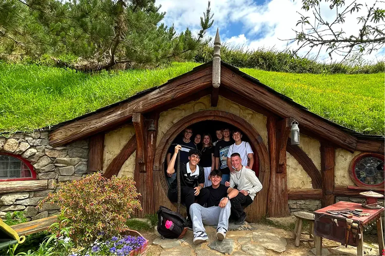 Gruppo di studenti in posa davanti alla porta rotonda di una casa hobbit a Hobbiton, in Nuova Zelanda