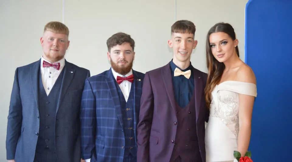 Quattro persone posano in abito formale davanti a uno sfondo blu nel campus dell'Athy College.
