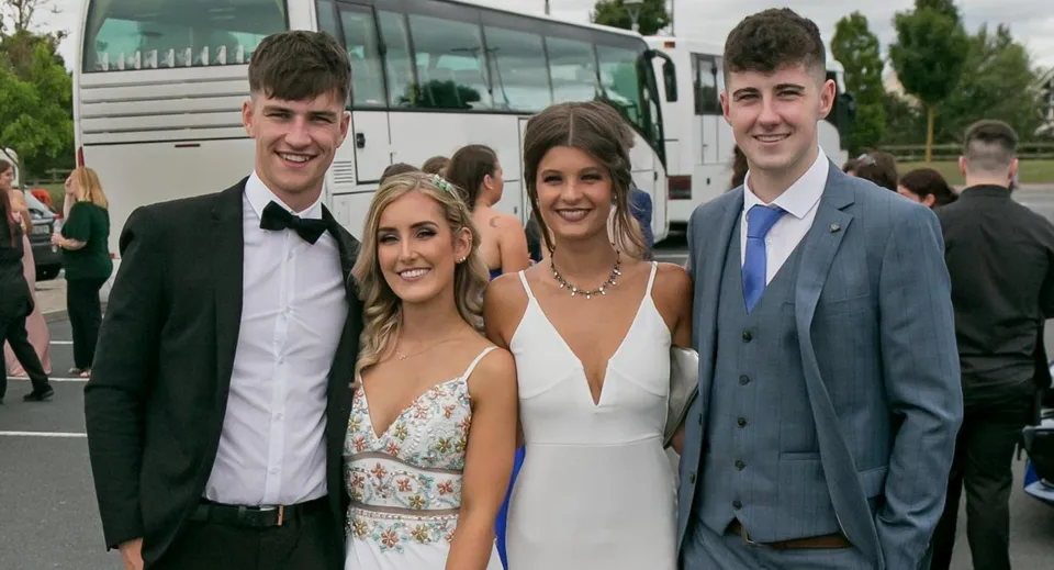 Quattro studenti della Scoil Dara in piedi davanti a un autobus in posa per una foto di gruppo in abbigliamento formale.