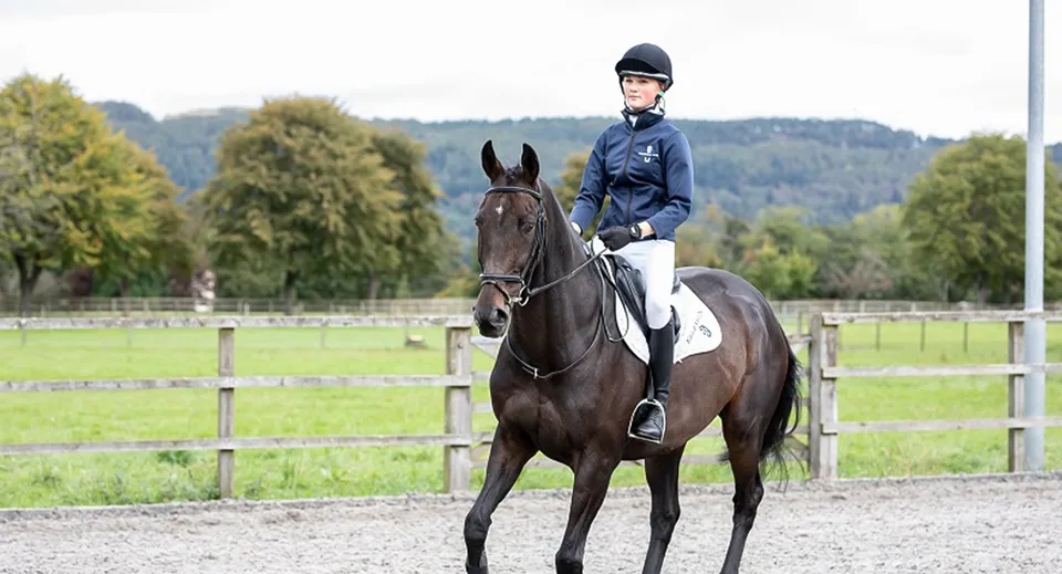 Una persona in abbigliamento da equitazione è a cavallo di un cavallo marrone nei terreni della Kilgraston School.