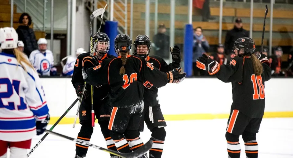 Giocatrici di hockey su ghiaccio della Kimball Union Academy con divise nere e arancioni festeggiano sulla pista.