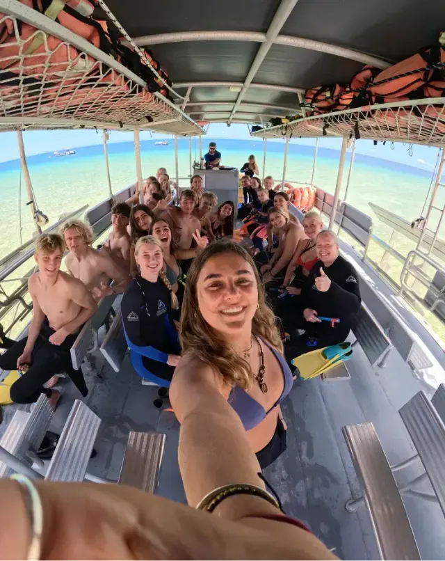 Gruppo di giovani in muta si fa un selfie su una barca prima di un'immersione nel mare tropicale
